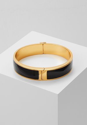 Bracelet jonc en or avec incrustation en émail noir, présenté sur un piédestal blanc avec un fond gris.
