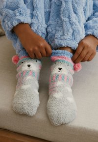 Szare, puszyste skarpetki z motywem misia, ozdobione kolorowymi paskami w różowym i niebieskim kolorze, z pomponami i miękką teksturą.