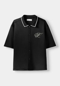 Czarna koszulka polo z krótkim rękawem, z białym obszyciem kołnierzyka, zapięciem na guziki z przodu oraz monogramem na lewej piersi.