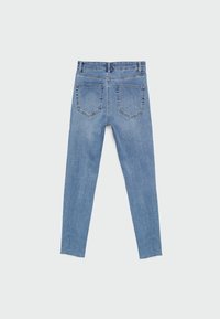 Vaqueros ajustados de denim de color azul claro con cintura alta, que presentan dos bolsillos traseros y un dobladillo sin terminar en los tobillos. Textura suave con leve desgaste.