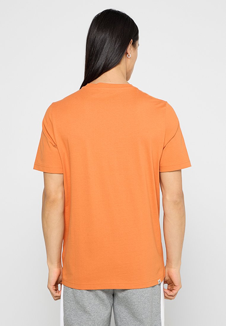 Camiseta de manga corta naranja, confeccionada en algodón, con cuello redondo y una textura suave. Presenta un pequeño detalle de logo en el lado inferior.