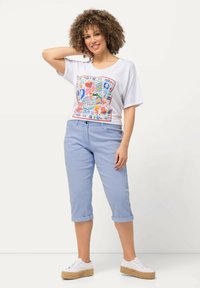 Camiseta blanca con estampado gráfico colorido, pantalones cortos de color azul claro y zapatos blancos con suela de esparto trenzada.