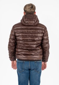 Bruine pufferjas met een capuchon, voorzien van horizontaal gestikte secties en een glanzend, textuur oppervlak, gecombineerd met blauwe jeans.