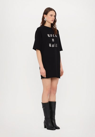 Vestido negro de gran tamaño con texto "Rock n Roll" en plateado, hecho de una tela suave. Combinado con botas de tacón negras hasta la rodilla.