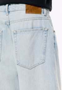Lyseblå denim jeans set bagfra, som viser en stor baglomme og et brunt lædermærkepatch over taljen.