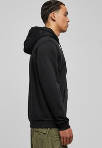 Sudadera negra de mezcla de algodón, con un bolsillo frontal, capucha con cordón y puños acanalados, combinada con pantalones cargo verdes oliva.
