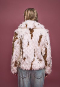 Vit och brun mönstrad fuskpälsjacka med en bred krage och fluffig textur, dragen över ljusblå denimjeans.