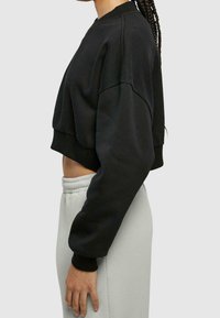 Felpa nera corta con scollatura rotonda, maniche larghe e polsini a coste, abbinata a pantaloni grigi chiari con elastico in vita.