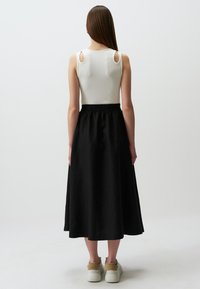 Zwarte midi-rok met een elastische tailleband, gecombineerd met een crèmekleurig tanktop met uitsnijdingen op de schouders. G gedragen met witte sneakers.