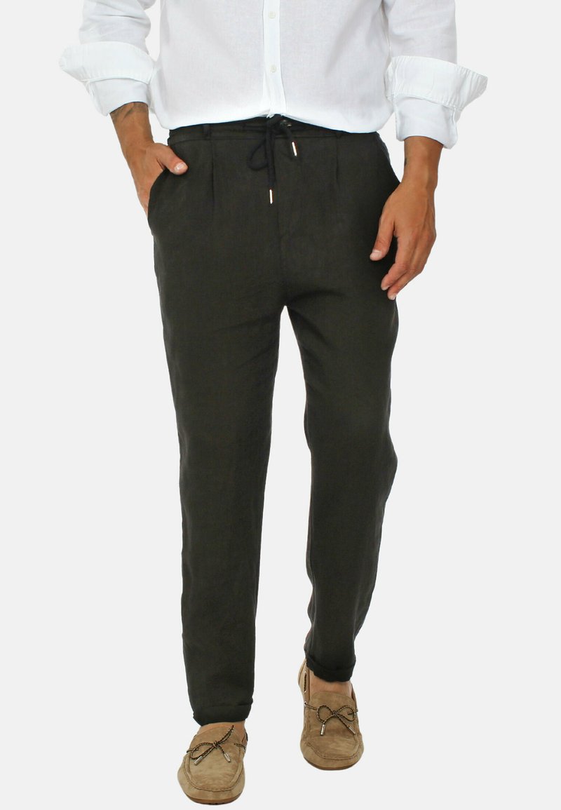 Pantaloni in lino neri dal taglio rilassato, con vita regolabile e tasche laterali. Abbinati a una camicia bianca con bottoni e scarpe color beige.