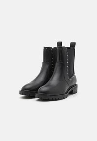Bottines en cuir noir avec des côtés élastiques, des accents cloutés, une semelle robuste et des languettes pour un enfilage facile.