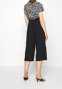 Zwarte culottes met een ontspannen pasvorm en cropped lengte, gecombineerd met een bloemetjesblouse met korte mouwen en een ronde hals.