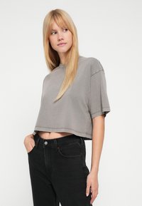 Camiseta gris recortada hecha de tela suave, con mangas cortas, escote redondo y detalles de costuras visibles, combinada con jeans negros.