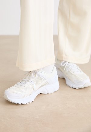White athletic shoes with a mesh design, textured surfaces, and supportive soles. Laces and subtle branding detail on the side.