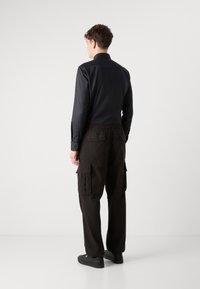 Zwarte lange mouwen shirt met een kraag, gecombineerd met zwarte cargo broek met zijzakken, elastische tailleband en instap zwarte schoenen.