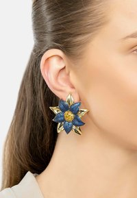 Gold and blue flower-shaped earrings, featuring textured blue petals, a golden center, and shiny gold accents. Large and bold design.