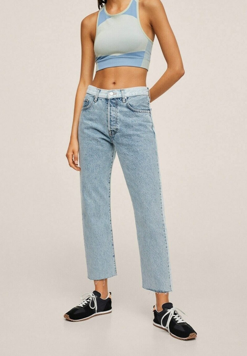 Pantalones vaqueros de mezclilla azul claro con corte recto y dobladillo deshilachado, combinados con un top deportivo azul claro recortado y zapatillas negras.