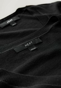 Schwarze Strickpullover mit V-Ausschnitt, versehen mit Etiketten mit der Aufschrift "NEXT". Weiche Textur, sichtbare gerippte Bündchen und feine Nähdetails.