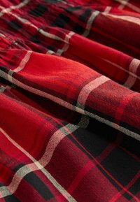 Tissu tartan à carreaux rouge, noir et blanc avec taille élastique froncée et texture douce en gros plan.