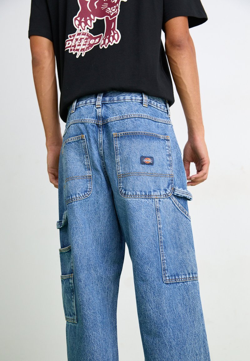 Hellblaue Denim-Cargo-Hosen mit lockerer Passform, mehreren Taschen und einem Patch am hinteren Taillenbund. Sie verfügen über kontrastierende Nähte.
