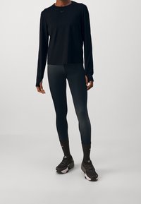 Černé tričko s dlouhým rukávem, elegantní tmavé legíny a černé sportovní boty. Materiály jsou lehké; design přiléhavý s minimálním značením.