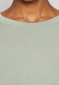Camiseta verde claro con cuello redondo, confeccionada en tejido suave. Presenta un cuello acanalado y una textura lisa y uniforme. No se observan patrones ni detalles.