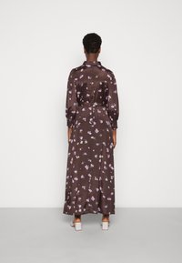 Langes braunes Blumenmaxikleid mit lila und weißen Blumenmustern, das über eine taillierte Taille, lange Ärmel und ein fließendes Design verfügt.