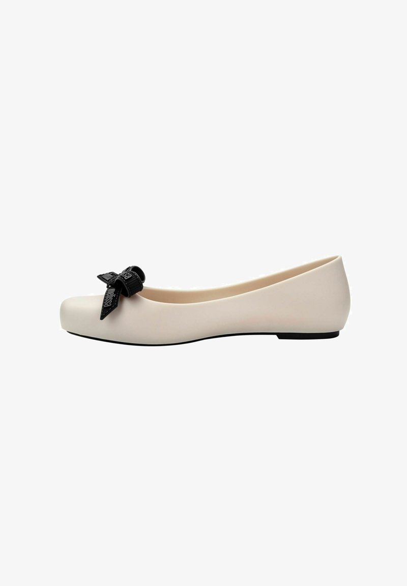 Bailarinas de color beige claro con punta redondeada, un lazo negro texturizado como acento y una suela negra plana. Acabado suave y mate.