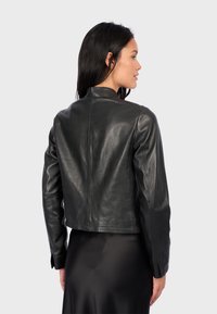 Black leather cropped jacket with a stand collar, smooth finish, long sleeves, and minimal stitching details, worn over a sleek garment.