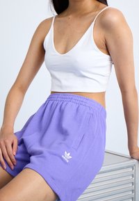 Vit kortbakad tanktop med bred halsringning, i kombination med ljuslila träningsshorts med elastiskt midjeband och sidofickor.