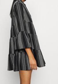 Robe à rayures noires et blanches avec des couches superposées, des manches évasées et des motifs à pois. Fabriquée dans un tissu à finition texturée.