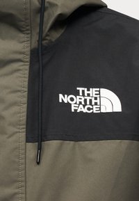 Χακί και μαύρο μπουφάν με κουκούλα, με κεντημένο λογότυπο στο στήθος. Λείο ύφασμα με ρυθμιζόμενα κορδόνια και λεπτομέρειες ραφής.