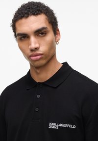 Črna polo majica iz mešanice bavlna, s klasičnim ovratnikom, tremi gumbi in vbodnim logotipom "KARL LAGERFELD JEANS" v beli barvi.