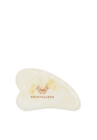 Strumento per il viso in cristallo con forma irregolare a cuore, realizzato in materiale chiaro; presenta una sottile texture e un logo in rilievo.