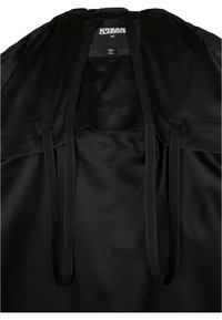 Vêtement en tissu en maille noir avec des cordons de serrage au cou et une étiquette intérieure cousue dans le col. Surface texturée avec un design respirant.