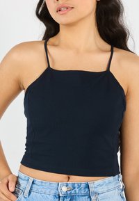 Marineblå, avkortet tanktop med tynne stropper, laget av teksturert stoff. Har firkantet utringning og figurnær fasong. Stilt med lyse denimshorts.
