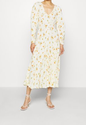 Mujer que lleva un vestido midi blanco con mangas largas y estampado floral, combinado con sandalias blancas de tiras con tacón.