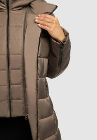 Rudas paminkštintas švarkas su aukštu apykakle, turintis užtrauktuką priekyje ir šoninėse kišenėse, pagamintas iš blizgaus, lygio audinio ir horizontalaus siuvimo.