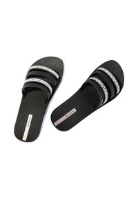 Czarne klapki na płaskiej podeszwie z dwoma lśniącymi paskami, teksturowaną podeszwą i akcentem z logo. Materiał wydaje się być gumowy lub syntetyczny.
