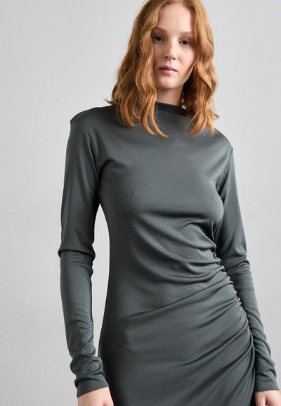 Long-sleeve, dark grey dress made of soft fabric with a mock neck; features gathered detailing along the side for added texture.
