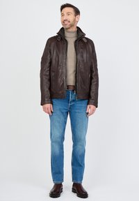 Bruine leren jas met een kraag, rits aan de voorkant en twee zijzakken. Gekleed over een beige coltrui en gecombineerd met een blauwe spijkerbroek en bruine laarzen.