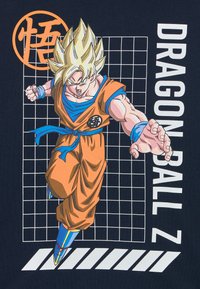 Narancs és kék grafikus póló, amelyen egy stilizált karakter látható a Dragon Ball Z-ből, sötétkék háttérrel, rácsmintával és szöveggel.