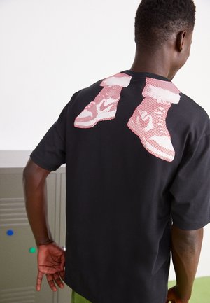 Maglietta nera in cotone con grafica di sneakers rosse e bianche sulla schiena, con maniche corte e vestibilità comoda.