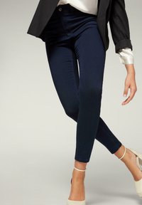 Pantalones vaqueros skinny azul marino con una textura suave y un diseño ajustado, que presentan un cierre frontal con botón y detalles de costura sutiles.