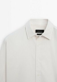 Chemise blanche à manches longues avec boutons, col classique et étiquette de marque noire à l'intérieur du col.