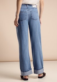 Jeans de mezclilla azul de pierna ancha con una cintura alta, que presentan dobladillos enrollados, bolsillos traseros y un acabado texturizado sutil.