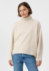 Beige Rollkragenpullover mit geripptem Kragen und Saum, mit lässiger Passform und langen Ärmeln, kombiniert mit blauen Jeans.