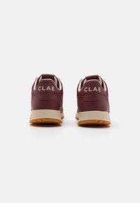 Maroon sneakers med texturerad läder, beige accenter och en gummiyttersula. "CLAE" märket på hälen. Låg toppdesign med en dragflik.