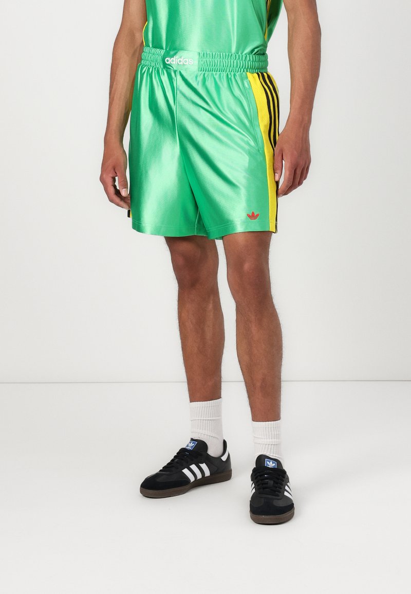 Žali satininiai šortai su geltonomis šoninėmis juostomis, elastinga juostele ir raudonu adidas logotipu. Derinami su juodais batais ir baltais kojinėmis.