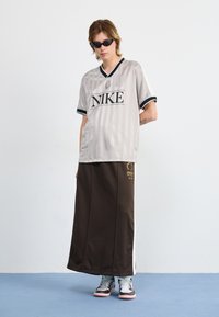 Nike horizontal striped gray athletic shirt with black accents and logo, paired with a long brown skirt featuring a graphic detail and white panel.